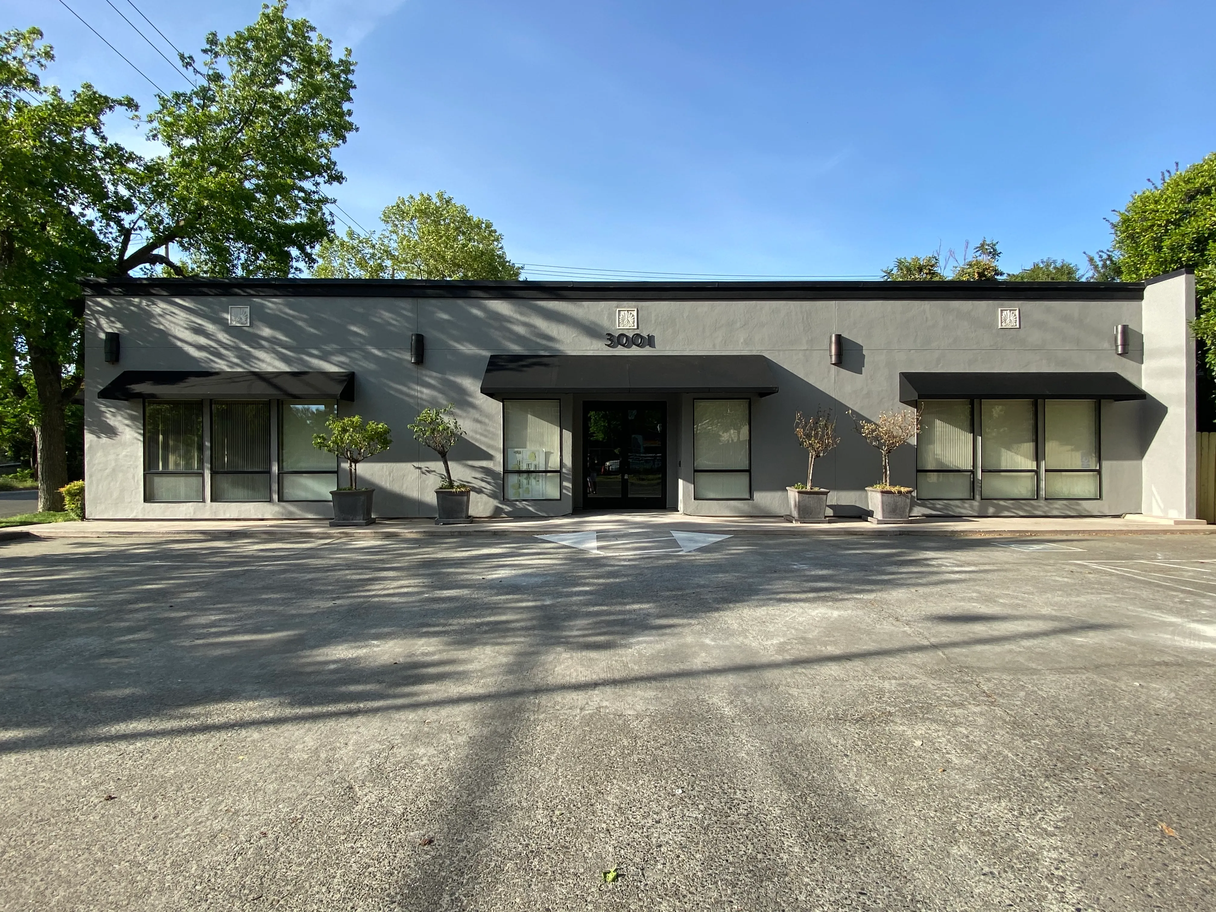 Renovated single-story office building at 3001 E Street Sacramento with dark gray stucco and black awnings - future site of multi-story mixed-use development