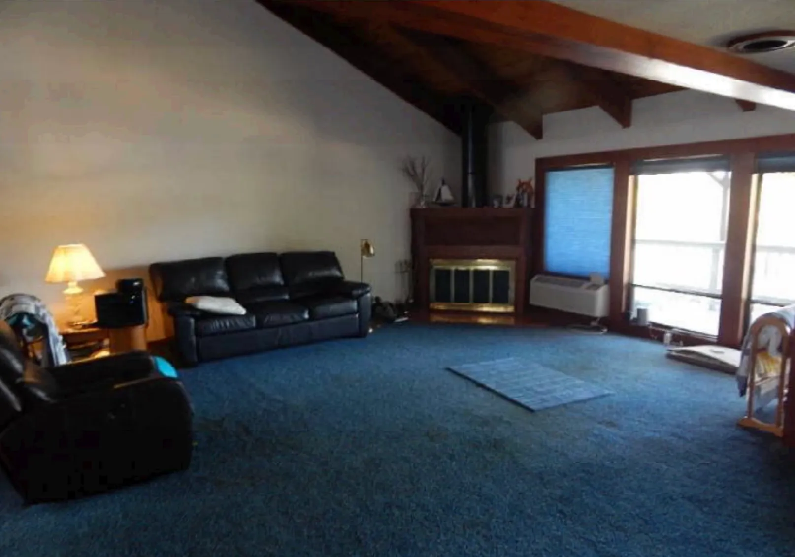Living room before renovation with blue carpet, dark wood ceiling, and dated corner fireplace