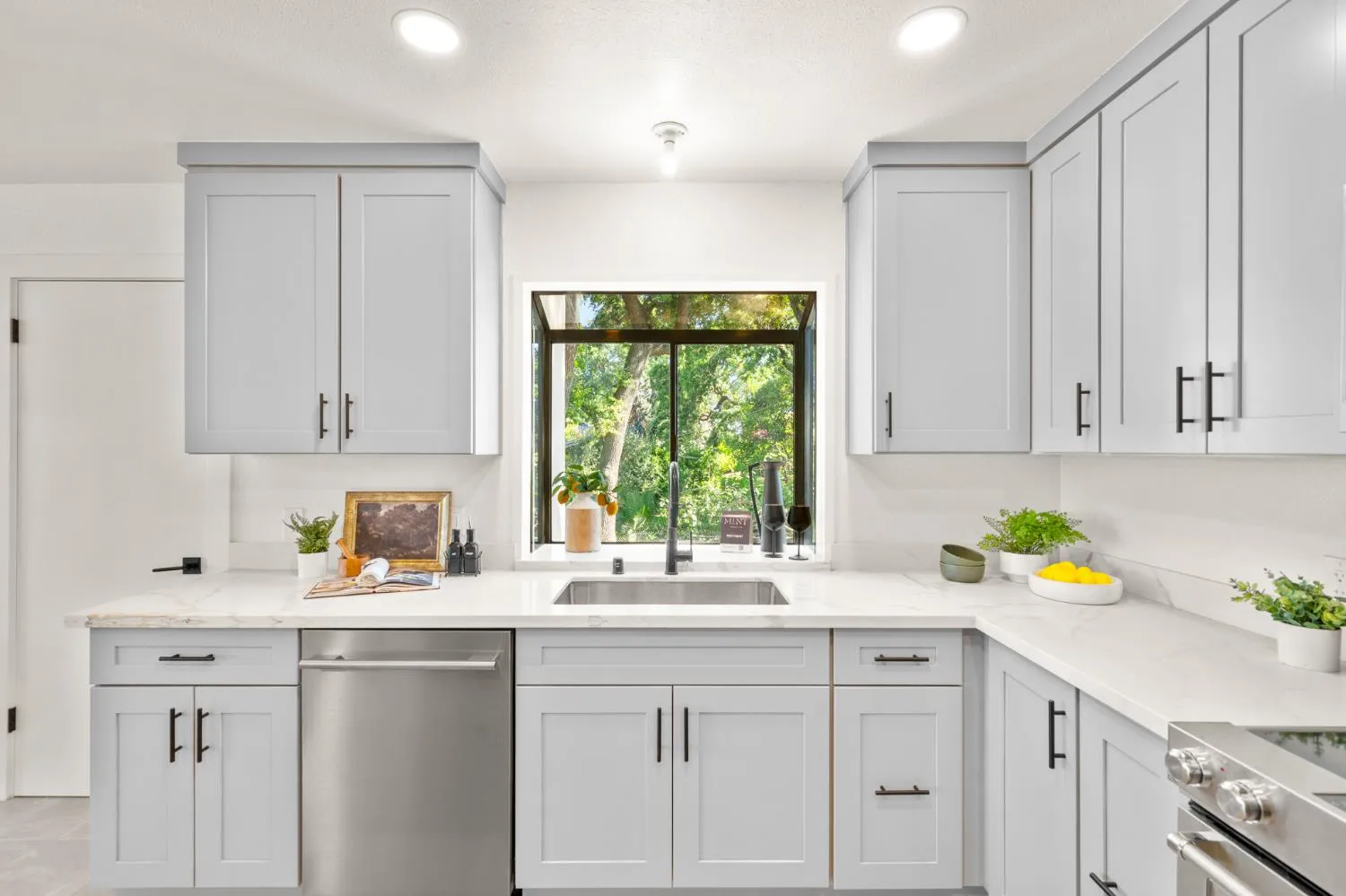 Renovated kitchen with light gray shaker cabinets, quartz counters, and garden window over the sink