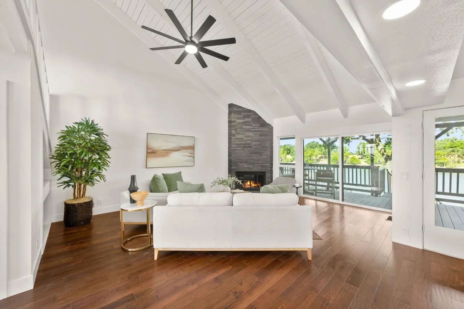 Renovated living room with white vaulted ceiling, stacked stone fireplace, and hardwood floors