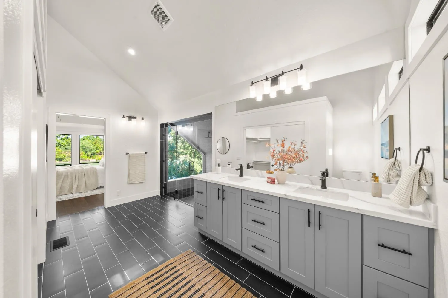 Primary bathroom with double vanity, marble-look counters, and dark tile floors