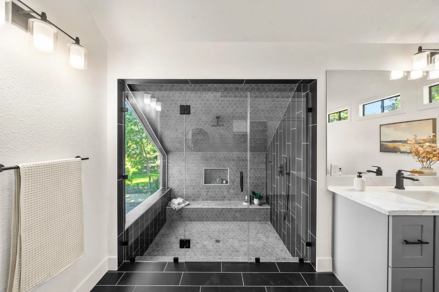 Renovated primary shower with hexagon tile, frameless glass, bench seating, and picture window