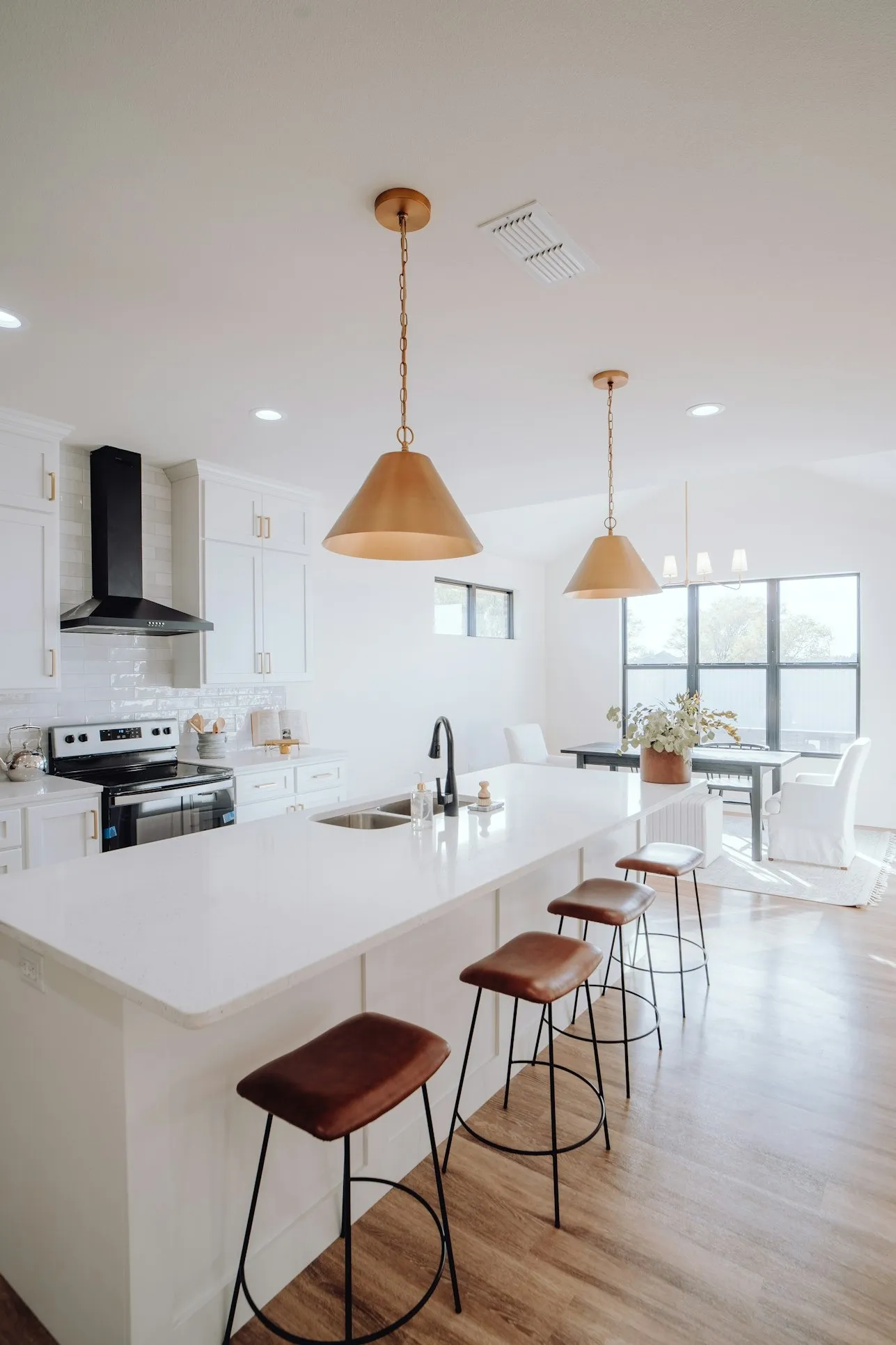 Bright open-concept kitchen with white quartz island, brass pendant lights, and leather bar stools on light wood flooring