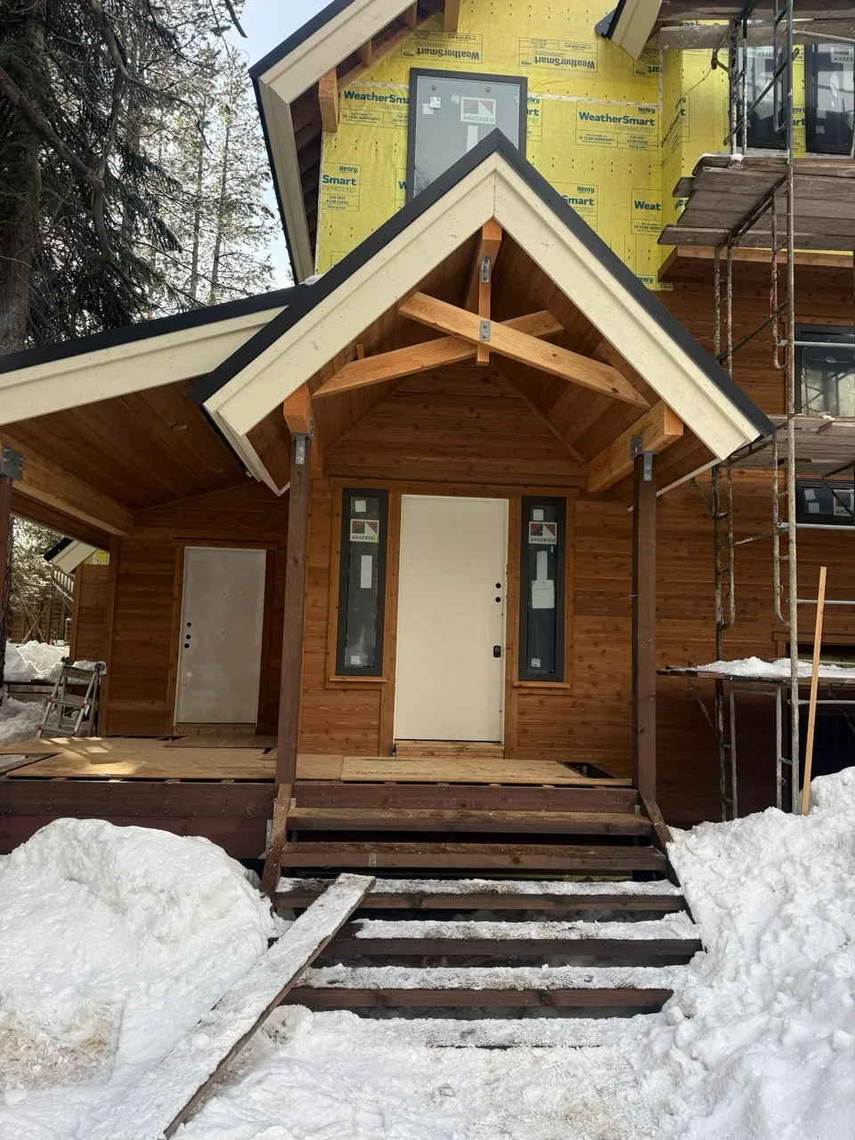 Timber gable entry porch with front door, sidelights, and wood steps during construction at the Soda Springs cabin