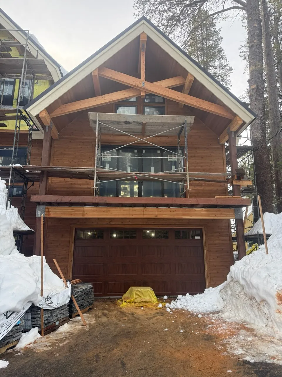 Close front view of Tahoe cabin showing timber frame, glass balcony railing, carriage house garage door, and surrounding pine trees