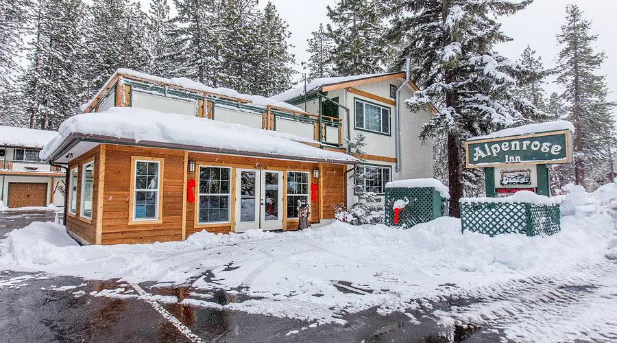 The former Alpenrose Inn in South Lake Tahoe - dated lodge with green signage and weathered wood exterior in snow